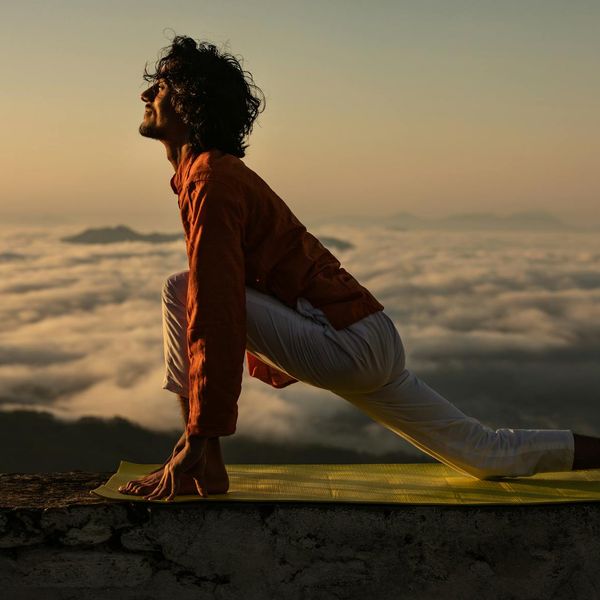 Silhouette of a person in a powerful yoga warrior pose at sunrise.